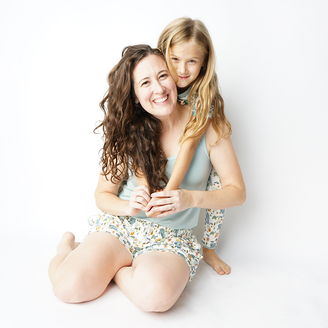 mother and daughter hugging each other. the daughter is wearing the manatee print in the 2-piece matching set. the mom is wearing the manatee women's shorts and the "blue surf" women's tank top. 