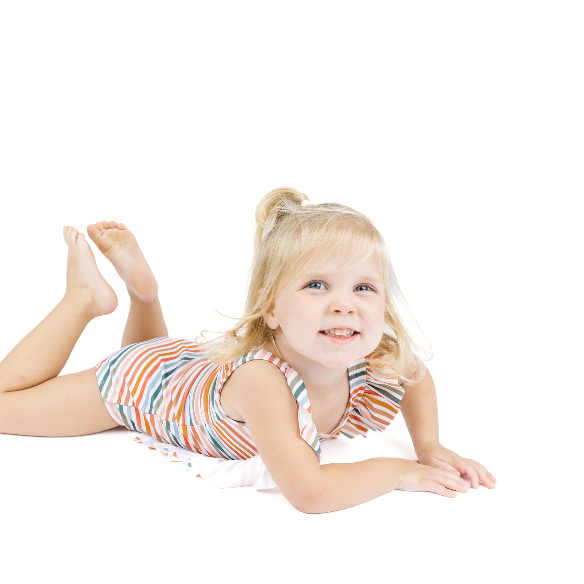 Young girl in a colorful striped dress lying on a white background
