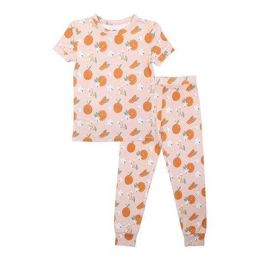 the 2-piece matching pajama set in the "freshly squeezed" print. the "freshly squeezed" print has an assortment of full and half cut oranges scattered around. there is also flower heads and flower stems that intermingle within the print. this is all space out around a pink background space. 