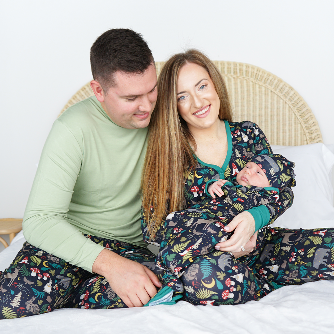 family of 3 in their "night forest" attire. mom is wearing the women's top. the "night forest" print is a night time themed design. you can see an array of forest animals ranging from, deer, bears, bunnies, birds, forest trees and leaves, flowers, and mushrooms. there are also starts and moons scattered around to enhance the night time atmosphere. 