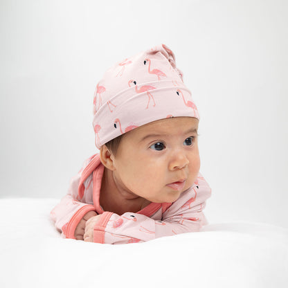 an infant in her "fancy flamingos" gown and hat, laying on her tummy. the "fancy flamingos" print is a pattern of multiple pink flamingoes scattered around the print. 
