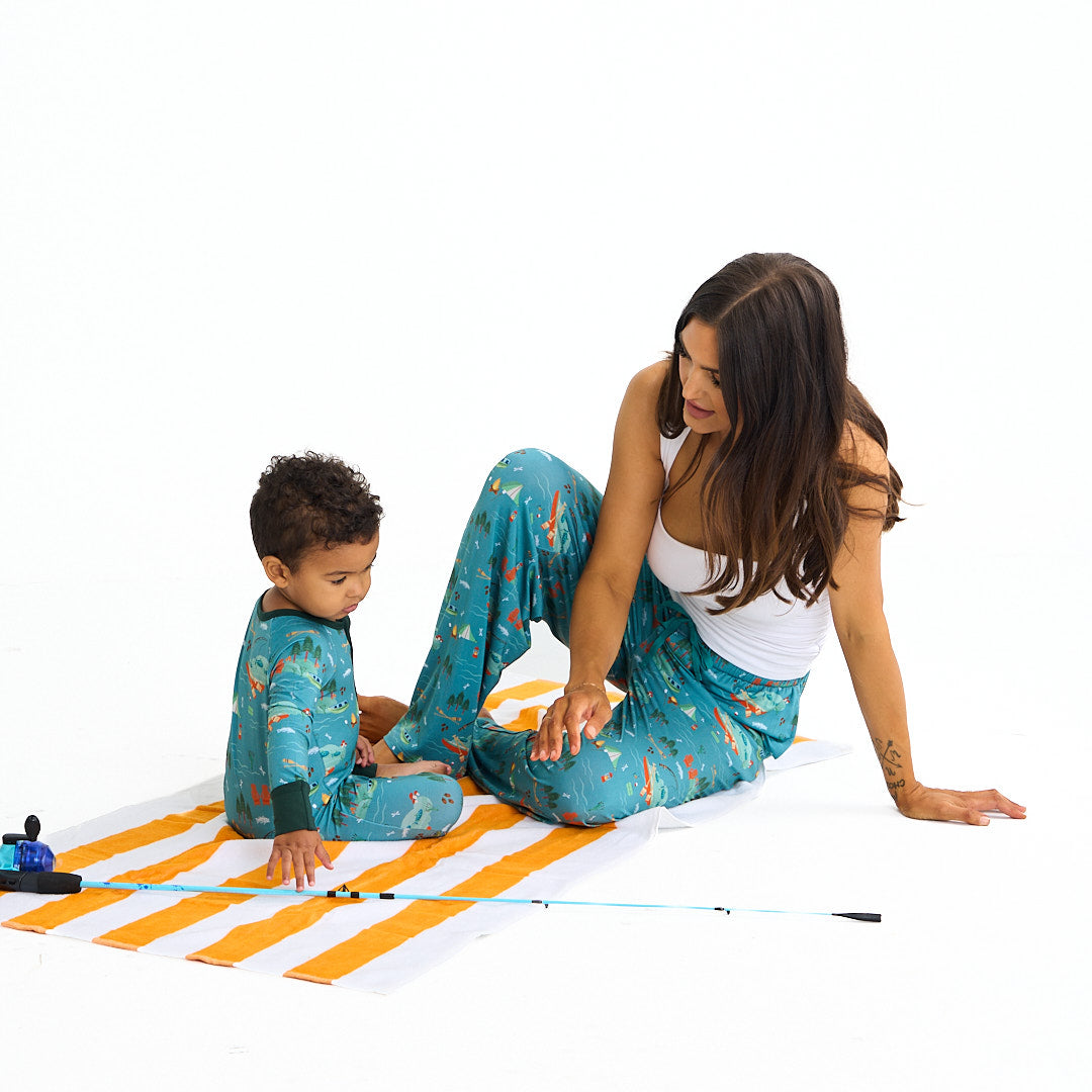 mom and son sit on a orange and white stripped towel. there is a kids fishing pole next to the boy. they both wear the "jump in the lake" apparel. the mom in the relaxed pants and the son in the convertible. the "jump in the lake" pattern is a print to capture the day in the life on a lake. you can fine fishing poles, tents, camp fires, adirondack chairs, marsh mellows, ores, canoes, forest trees, and different types of fish and fishing gear.