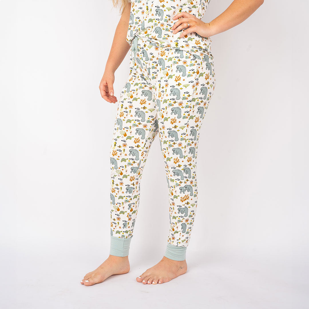 woman poses in her "manatee" bamboo joggers and women's top. the print "manatee" unites the florida sea life in a majestic print. there is a variation of florida manatees, yellow and pink sea horses, yellow and pink starfish, bubbles, turtles, and coral patterned across a white background