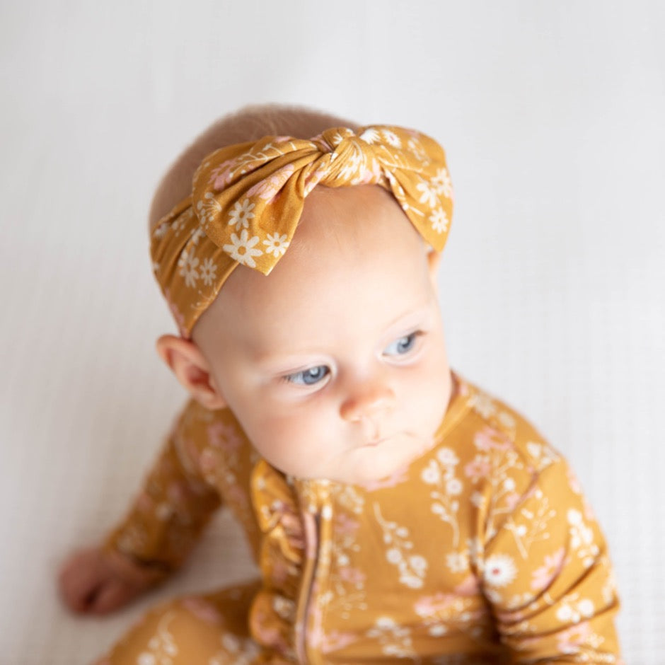 zoomed in and focused photo of a baby wearing the "mustard floral" baby headband. the "mustard floral" print are a bunch of white and pink floral flowers on a mustard yellow background. 