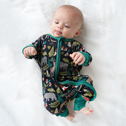 a infant baby lays on their back on a white blanket. the baby is wearing the "night forest" convertible. the "night forest" print is a night time themed design. you can see an array of forest animals ranging from, deer, bears, bunnies, birds, forest trees and leaves, flowers, and mushrooms. there are also starts and moons scattered around to enhance the night time atmosphere. 