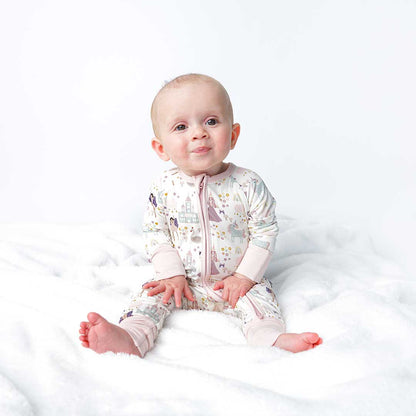 a happy baby sits on a white blanket. the baby wears the "once upon a time" convertible. the "once upon a time" print is a mix of pinks, purples, whites, blues, and yellows. you can see fairy princess and regular princess, unicorns, swans, and castles. theres also hearts, stars and sparkles scattered around the print. 