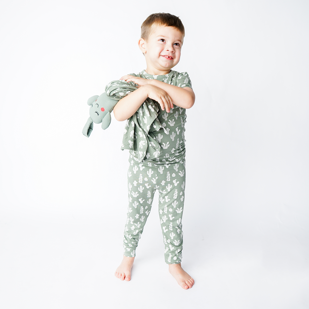 a young boy in the "stay sharp" matching pajama set, holds the "stay sharp" lovey. the "stay sharp" print is a variety of different white cacti on a greyish/green background. 