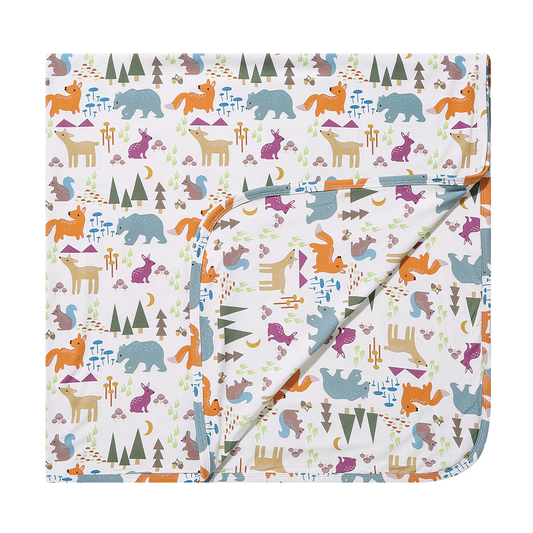 the "forest friends" bamboo blanket. the "forest friends" print has a mix of red foxes, brown deer, blue bears, purple bunnies, trees, grass, mushrooms, acorns, moons, and other colored dots scattered over a white background. 