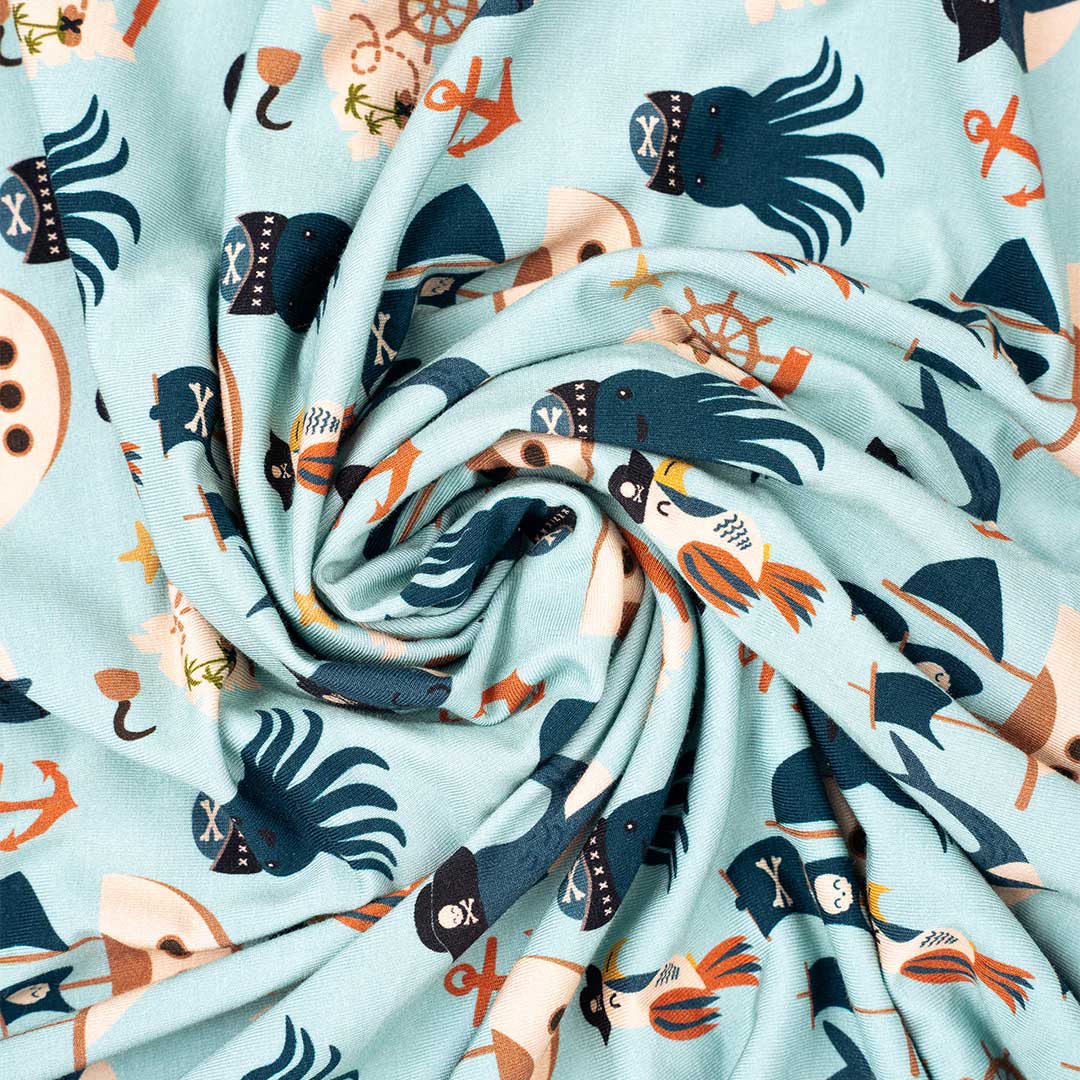 the "pirate's life" bamboo blanket. the "pirate's life" print is a mix of octopus, whales, and seagulls all wearing pirate hats. there are also anchors, pirate ships, treasure maps, and starfish mixed into the pattern. this is all displayed on a teal background. 