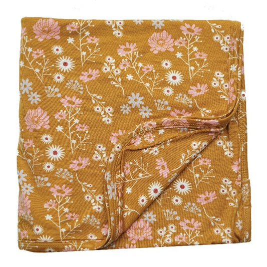 the "mustard floral" bamboo blanket. the "mustard floral" print are a bunch of white and pink floral flowers on a mustard yellow background. 