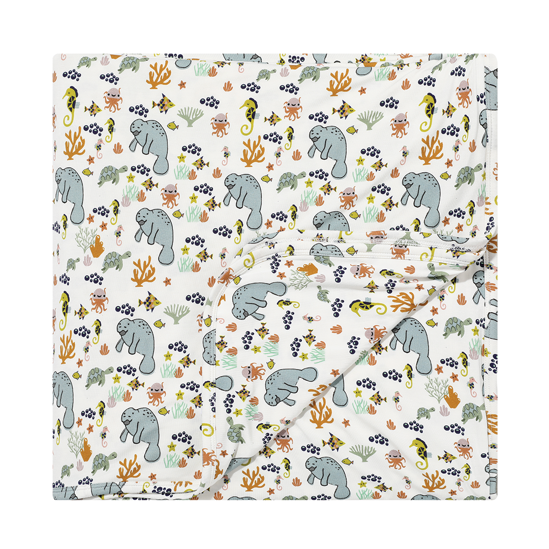 the "manatee" bamboo blanket. the print "manatee" unites the florida sea life in a majestic print. there is a variation of florida manatees, yellow and pink sea horses, yellow and pink starfish, bubbles, turtles, and coral patterned across a white background