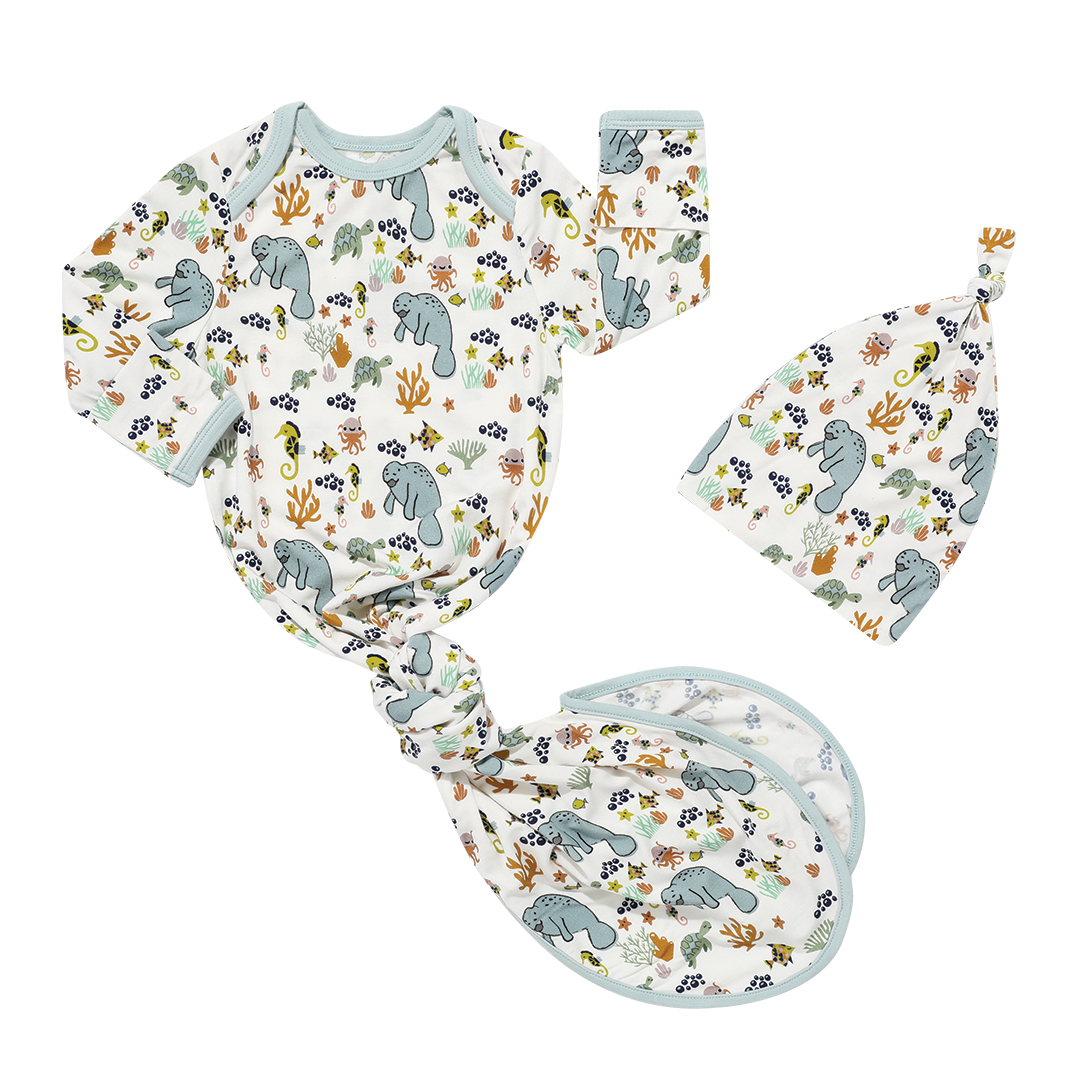 the "manatee" gown and hat set. the gown is tied in a knot at the bottom. the print "manatee" unites the florida sea life in a majestic print. there is a variation of florida manatees, yellow and pink sea horses, yellow and pink starfish, bubbles, turtles, and coral patterned across a white background