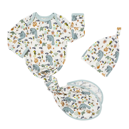 the "manatee" gown and hat set. the gown is tied in a knot at the bottom. the print "manatee" unites the florida sea life in a majestic print. there is a variation of florida manatees, yellow and pink sea horses, yellow and pink starfish, bubbles, turtles, and coral patterned across a white background