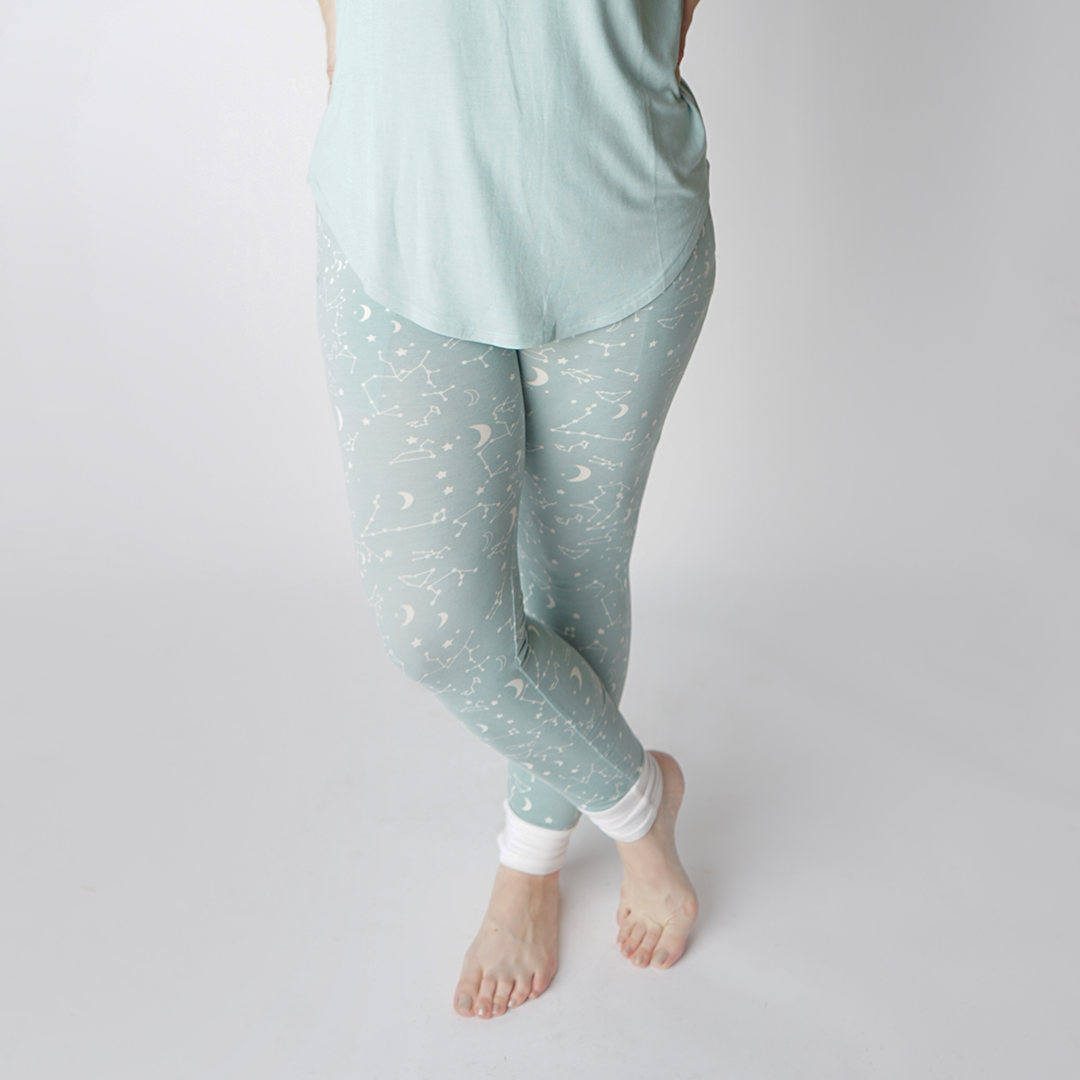 a close up of a women wearing the "stargazer" women's joggers. her legs are crossed in this photo. the "stargazer" print is a baby blue background with a mix of moons, constellations, and stars.