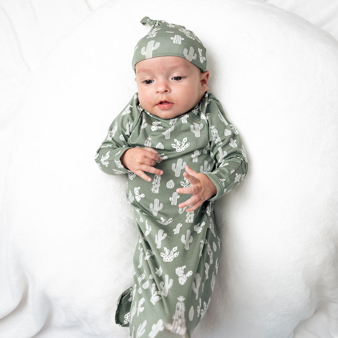 infant baby lays on a white pillow. the baby is in the "stay sharp" gown and hat set. 