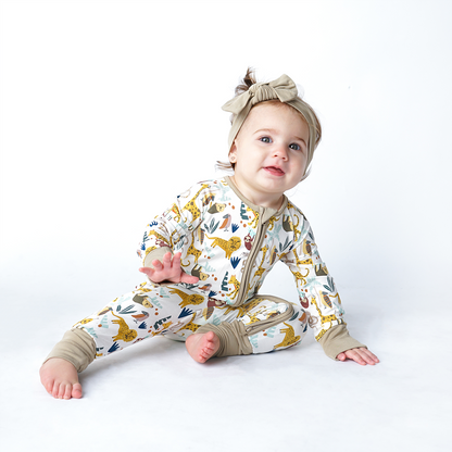 baby girl sits on the floor in her "jungle friends" convertible and headband. the "jungle friends" print is a mix of jungle animals that include giraffes, lions, cheetahs, sloths, snakes, and forest plants. 