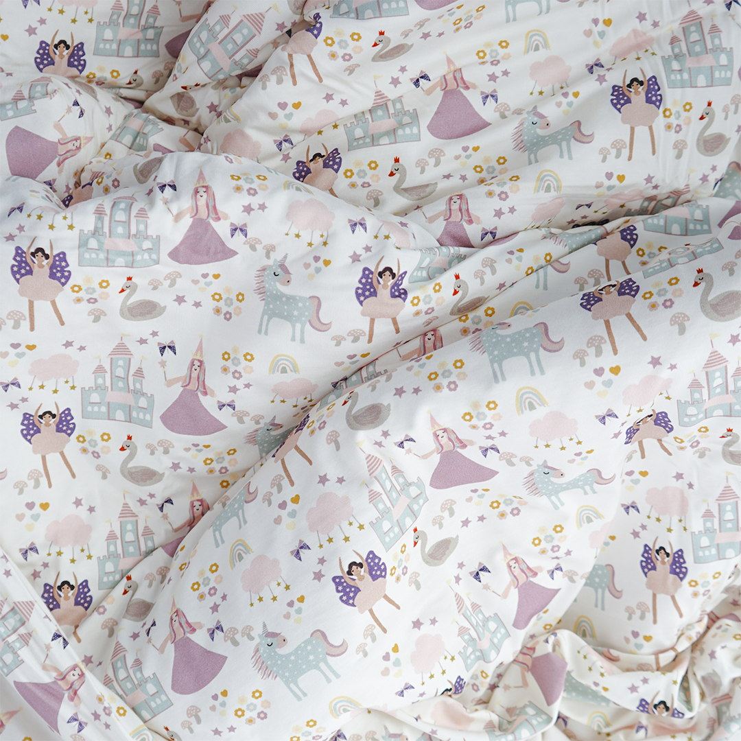 a close up of the "once upon a time" bamboo blanket. the "once upon a time" print is a mix of pinks, purples, whites, blues, and yellows. you can see fairy princess and regular princess, unicorns, swans, and castles. theres also hearts, stars and sparkles scattered around the print. 