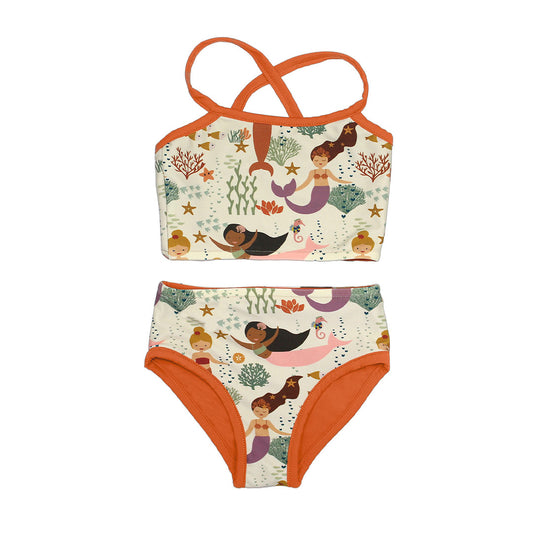 the "making waves" mermaids and light coral reversible bikini. the "making waves" print has a diverse spread of mermaids, sea coral, starfish, fish, and bubbles all spread out in different colors. this is all put on a beige background.