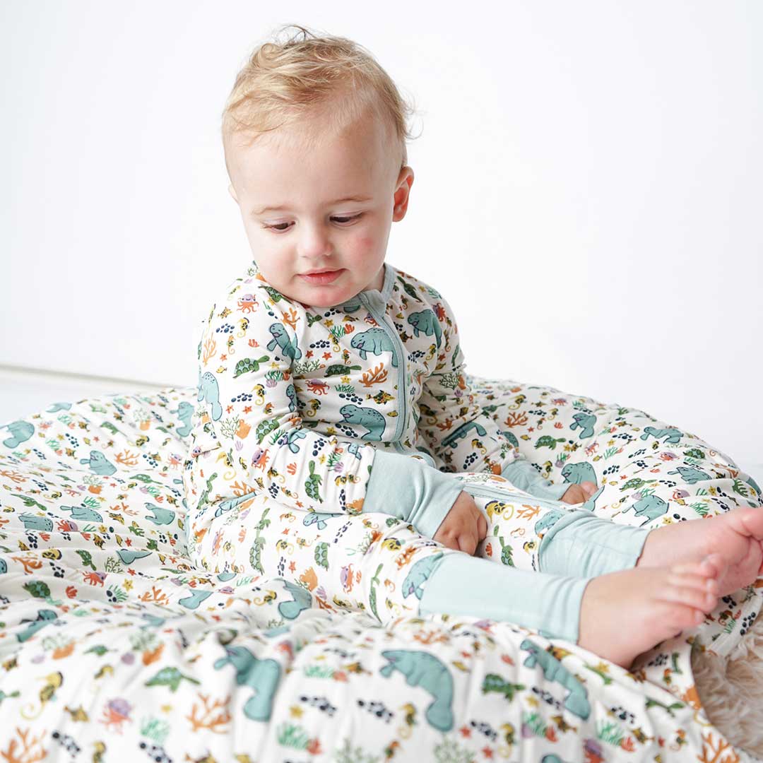 a little boy sits on the "manatee" blanket in his "manatee" convertible. the print "manatee" unites the florida sea life in a majestic print. there is a variation of florida manatees, yellow and pink sea horses, yellow and pink starfish, bubbles, turtles, and coral patterned across a white background