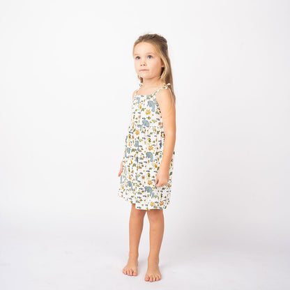 a girl stands looking at the sky in her "manatee" sundress. the print "manatee" unites the florida sea life in a majestic print. there is a variation of florida manatees, yellow and pink sea horses, yellow and pink starfish, bubbles, turtles, and coral patterned across a white background