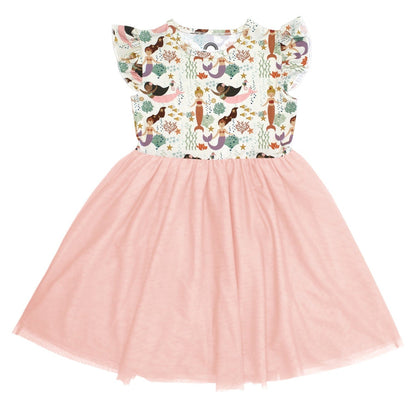 the "making waves" tulle twirl dress. this dress has the "making waves" print on the top half and a light pink bottom half. the "making waves" print has a diverse spread of mermaids, sea coral, starfish, fish, and bubbles all spread out in different colors. this is all put on a beige background.