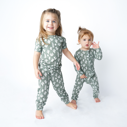 2 girls stand and look at the camera. the older girl is in the "stay sharp" matching pajama set. the younger girl next to her, wears the "stay sharp" convertible. the "stay sharp" print is a variety of different white cacti on a greyish/green background. 