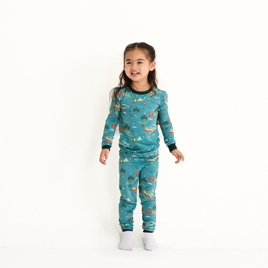 young girl stands and poses for the camera. she wears the "jump in the lake" matching pajama set. the "jump in the lake" pattern is a print to capture the day in the life on a lake. you can fine fishing poles, tents, camp fires, adirondack chairs, marsh mellows, ores, canoes, forest trees, and different types of fish and fishing gear.