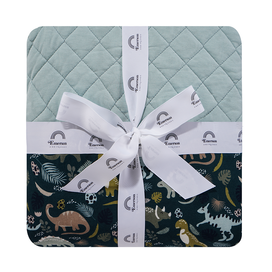 the "prehistoric friends" twin quilt. the "prehistoric friends" print is a mix of cute dinosaurs, eggs, and branches, all scattered on a dark green background.