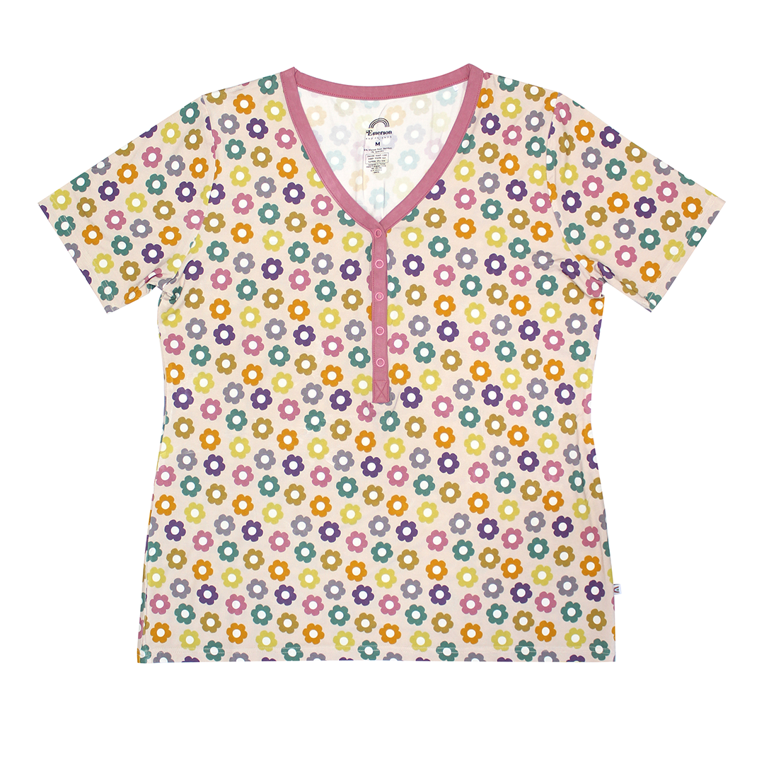 the "feeling groovy" women's top. the "feeling groovy" print is a flowered print in multiple colors. these flowers are retro and groovy. the background is light pink. 