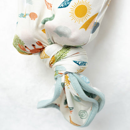the bottom half of the gown tied at the bottom in a knot. the "beach days" print is a scattered print of beach umbrellas, beach balls, sand buckets and shovels, coral, shells, beach chairs, seagulls, flipflops, and sunglass mixed in a orderly and creative way. 