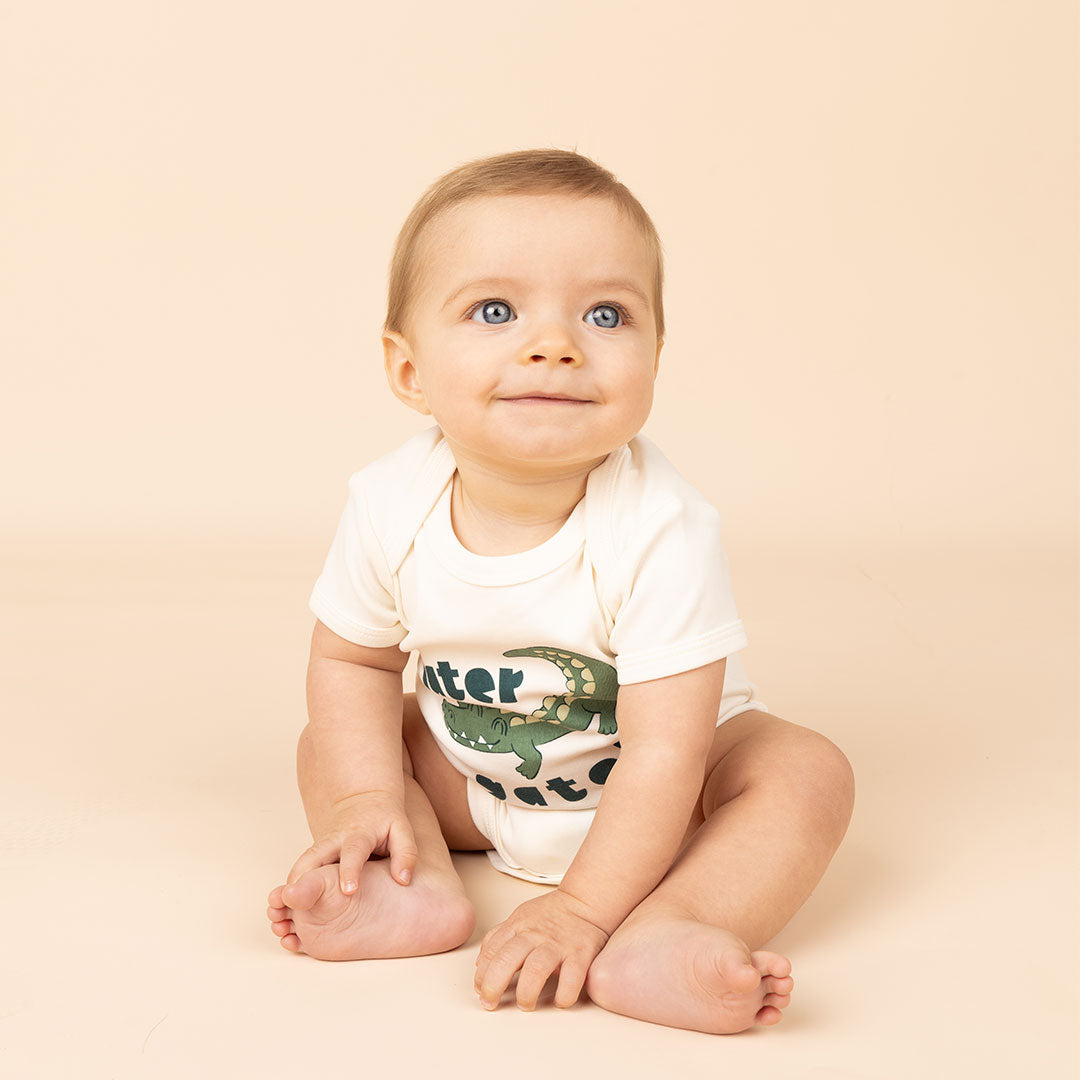 a smiling baby in the "later gator" cotton onesie. this design says "later gator" with a alligator across it. 