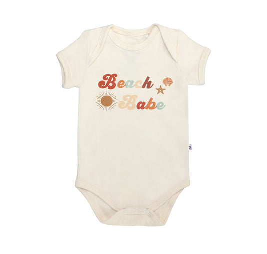 the "beach babe" cotton onesie. the word 'beach babe' is spelt out in a groovy font with a sun, starfish, and shell surrounding it. 
