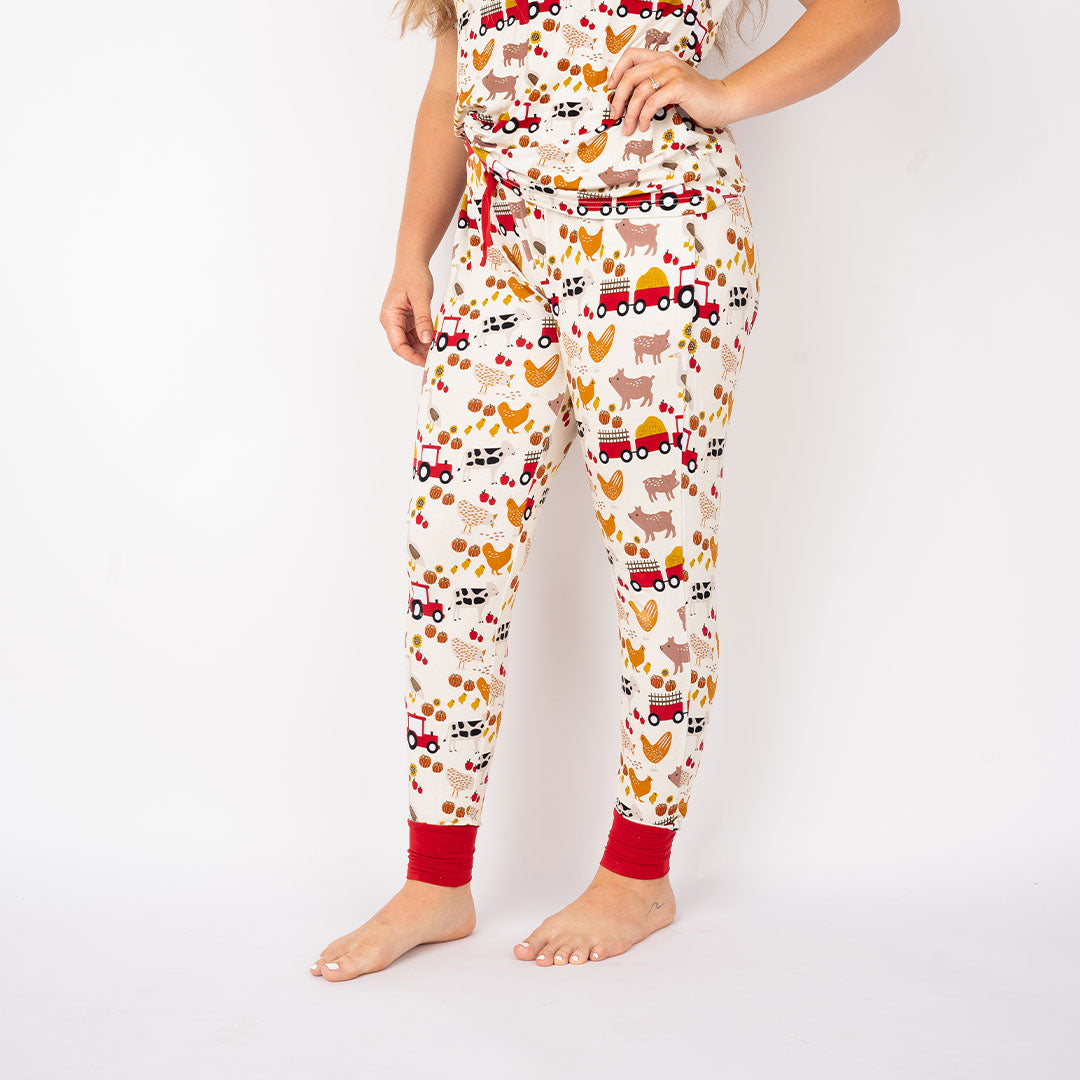 the bottom half of a women posing with her hand on her hip. she is wearing the "farm friends" women's joggers. the "farm friends" print is a collection of chickens, roosters, pigs, bails of hay, tractors, chicks, apples, and pumpkins. it's a white background and flashed of reds, yellows, and oranges, to bring out the farm aesthetic.