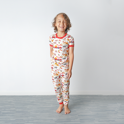 a girl stands and laughs at the camera. she is wearing the "farm friends" matching pajama set. the "farm friends" print is a collection of chickens, roosters, pigs, bails of hay, tractors, chicks, apples, and pumpkins. it's a white background and flashed of reds, yellows, and oranges, to bring out the farm aesthetic.
