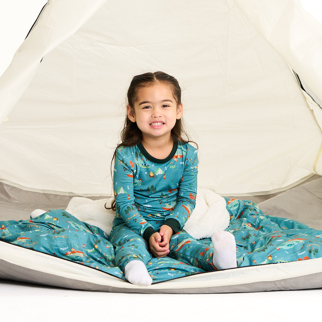 little girl sits on the "jump in the lake"  fleece blanket inside a tent. she wears the "jump in the lake" matching pajama set. the "jump in the lake" pattern is a print to capture the day in the life on a lake. you can fine fishing poles, tents, camp fires, adirondack chairs, marsh mellows, ores, canoes, forest trees, and different types of fish and fishing gear.