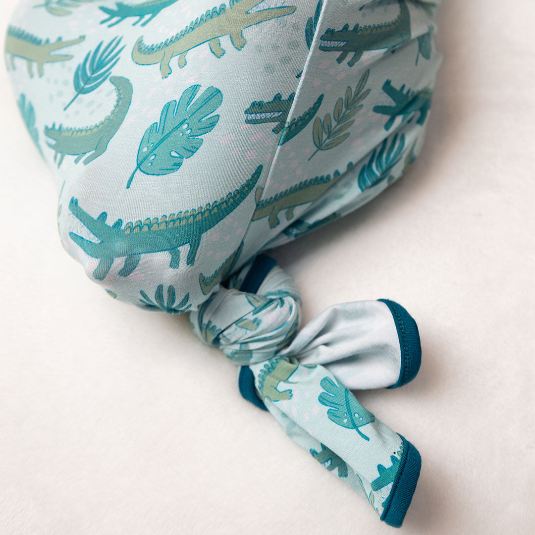 the bottom half of the "later gator" gown with a tie at the bottom. the "later gator" print has a mix of light and dark green alligators, leaves, and white dots scattered on a teal colored background. 