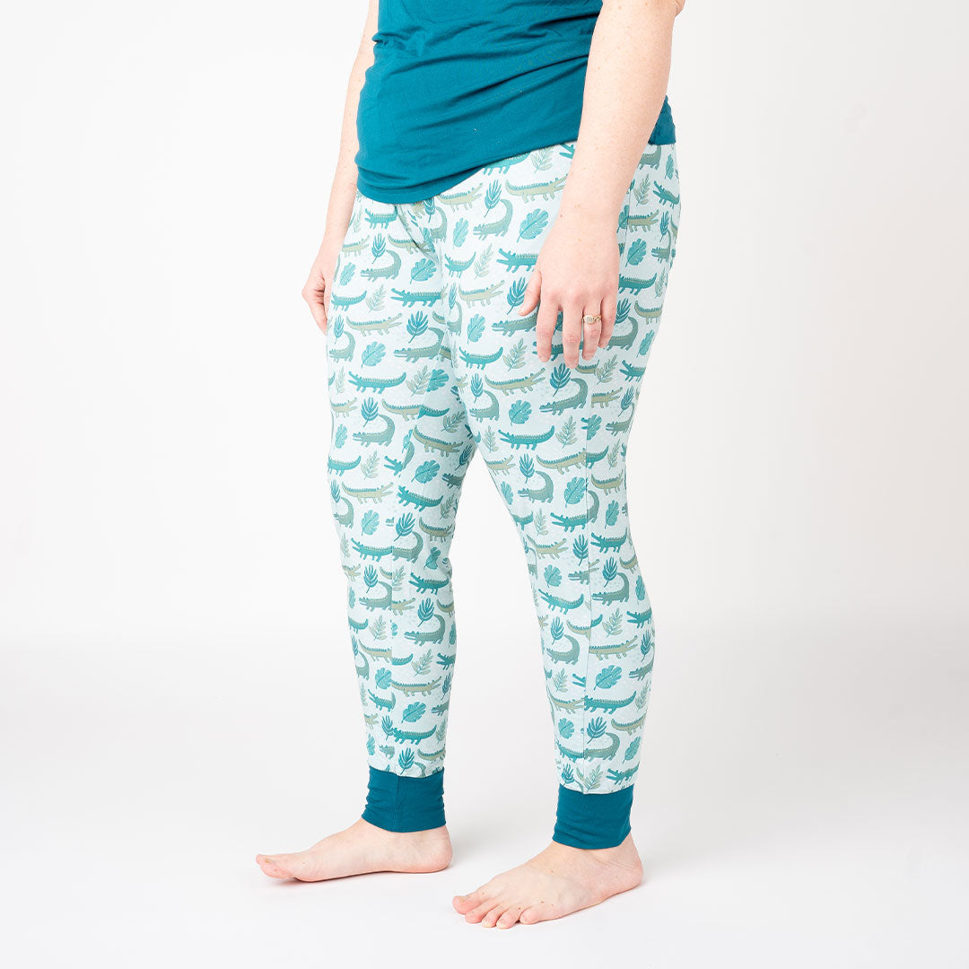 person in their "later gator" joggers. the "later gator" print has a mix of light and dark green alligators, leaves, and white dots scattered on a teal colored background. 