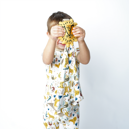 a young boy guards his face with the "jungle friends" lion lovey. the boy wears the 2-piece matching pajama set. the "jungle friends" print is a mix of jungle animals that include giraffes, lions, cheetahs, sloths, snakes, and forest plants. 