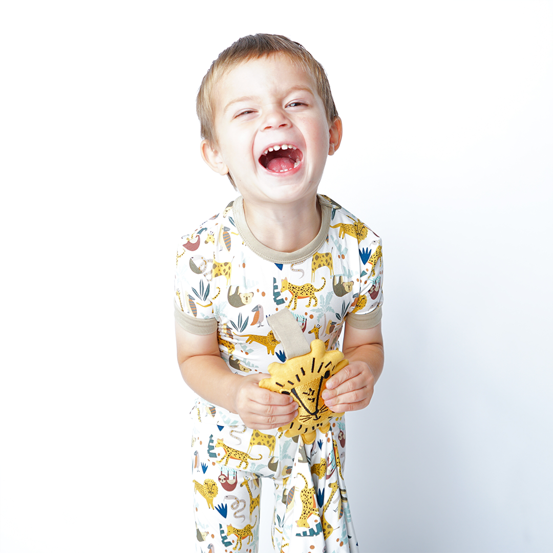 a little boy wears the "jungle friends" matching pajama set. he holds the lion lovey. the "jungle friends" print is a mix of jungle animals that include giraffes, lions, cheetahs, sloths, snakes, and forest plants. 