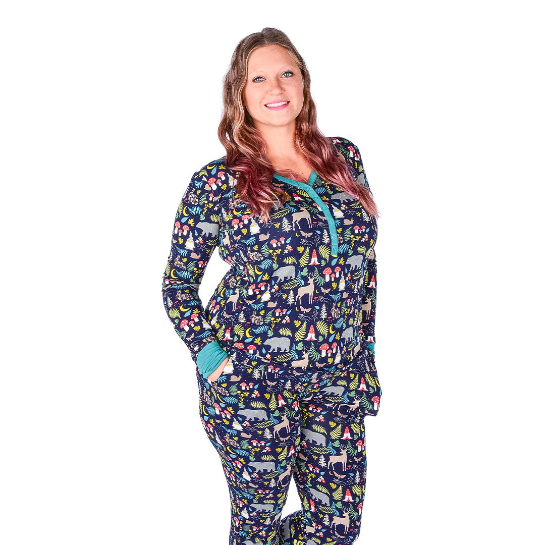 women poses with her hands in the pockets of the "night forest" women's joggers. she is also wearing the "night forest" women's top. the "night forest" print is a night time themed design. you can see an array of forest animals ranging from, deer, bears, bunnies, birds, forest trees and leaves, flowers, and mushrooms. there are also starts and moons scattered around to enhance the night time atmosphere. 