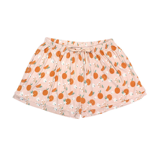 the "freshly squeezed" women's bamboo pajama shorts. the "freshly squeezed" print has an assortment of full and half cut oranges scattered around. there is also flower heads and flower stems that intermingle within the print. this is all space out around a pink background space. 