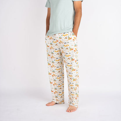 a man posing in the "beach days" relaxed pants. his hands are in the pockets of the pants. the "beach days" print is a scattered print of beach umbrellas, beach balls, sand buckets and shovels, coral, shells, beach chairs, seagulls, flipflops, and sunglass mixed in a orderly and creative way. 