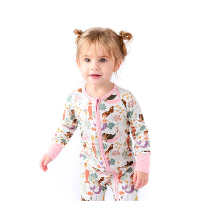 cute toddler girl stands in her "making waves" convertible. the "making waves" print has a diverse spread of mermaids, sea coral, starfish, fish, and bubbles all spread out in different colors. this is all put on a beige background.