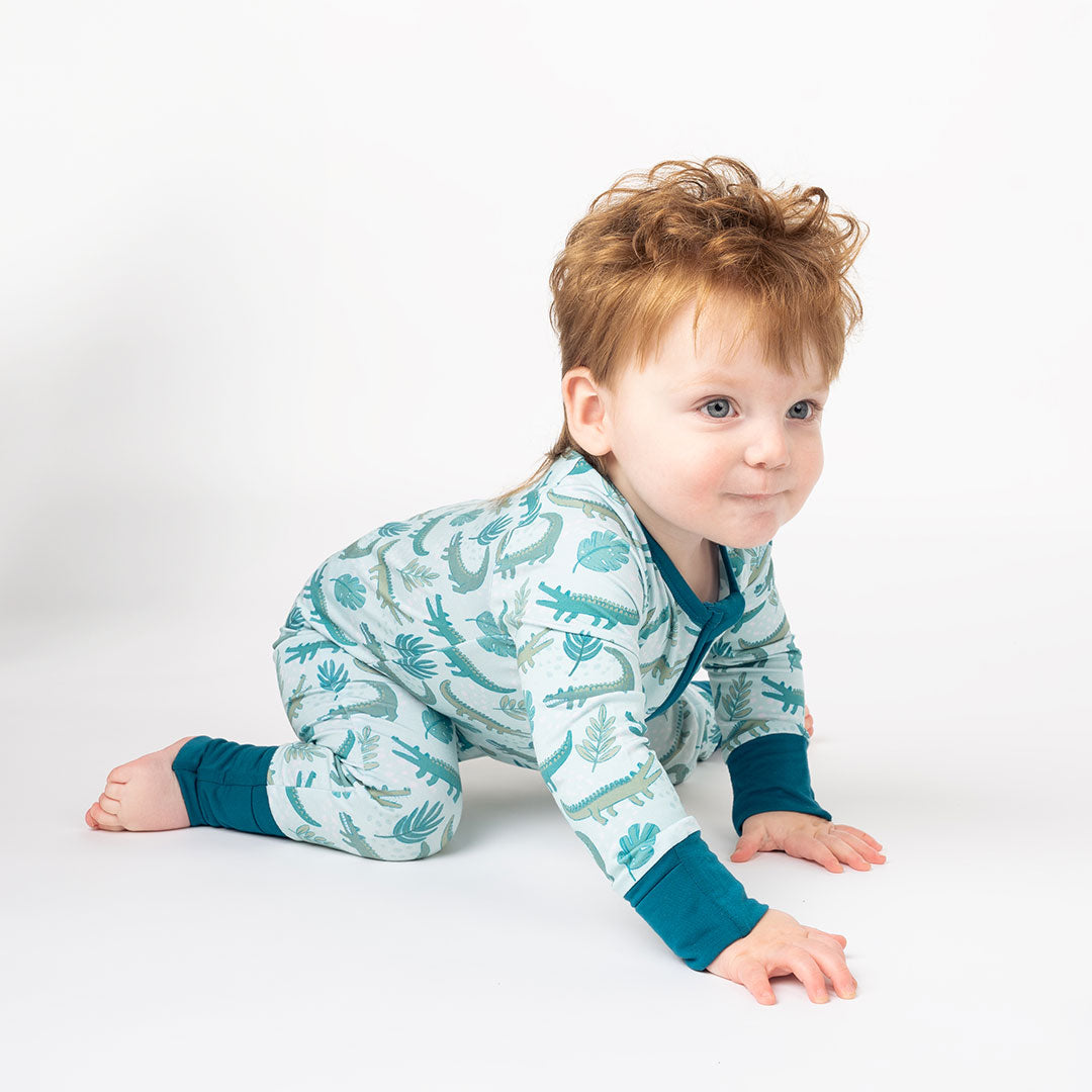 little toddler boy crawling around, wearing his "later gator" convertible. the "later gator" print has a mix of light and dark green alligators, leaves, and white dots scattered on a teal colored background. 