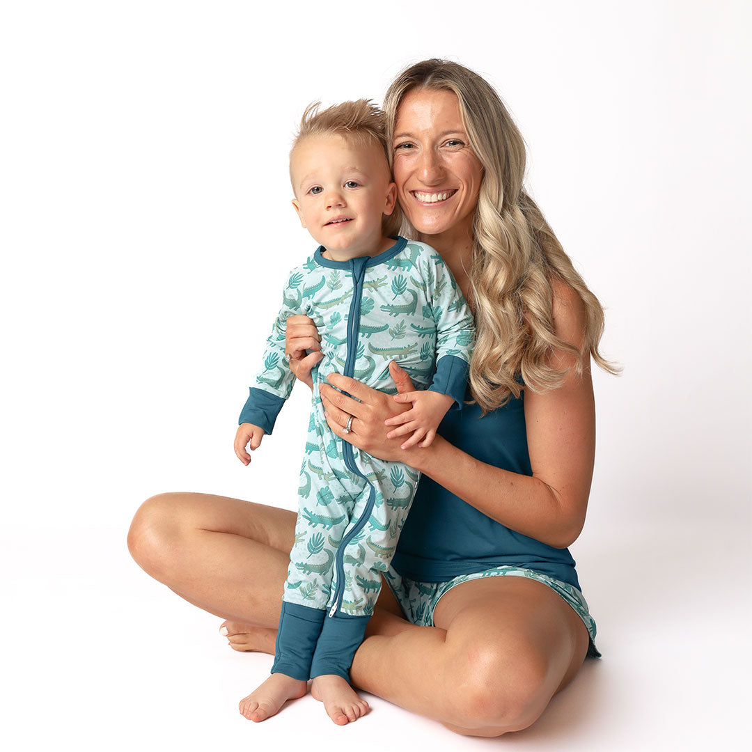 mom and son posing in their "later gator" apparel. the "later gator" print has a mix of light and dark green alligators, leaves, and white dots scattered on a teal colored background. 