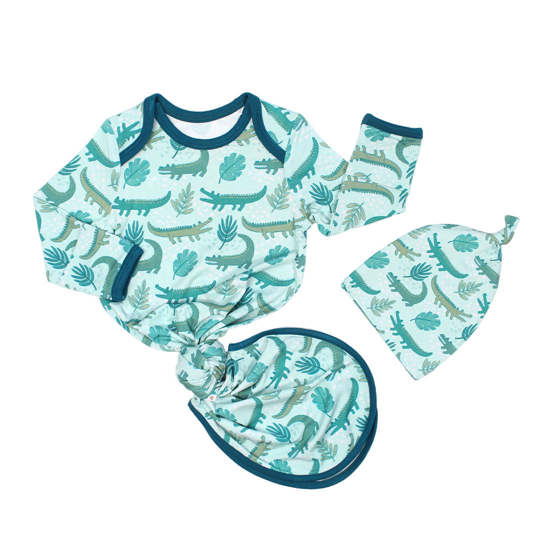 the "later gator" gown and hat set. the "later gator" print has a mix of light and dark green alligators, leaves, and white dots scattered on a teal colored background. 