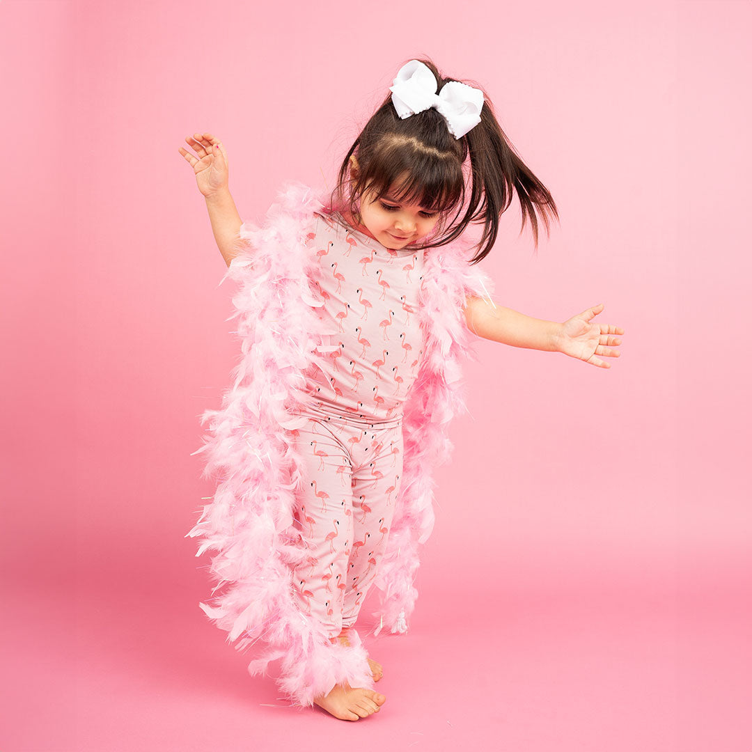 a cute toddler girl playing in her "fancy flamingos" 2-piece matching set. she is wearing a feathered boa scarf. the "fancy flamingos" print is a pattern of multiple pink flamingoes scattered around the print. 