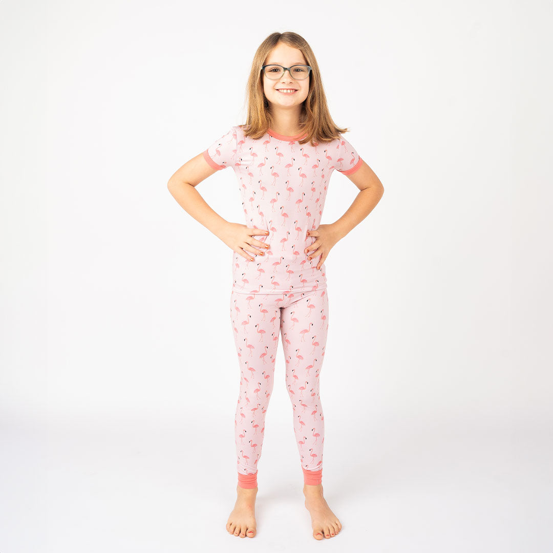 a young girl posing in her "fancy flamingos" matching 2-piece pajama set. the "fancy flamingos" print is a pattern of multiple pink flamingoes scattered around the print. 