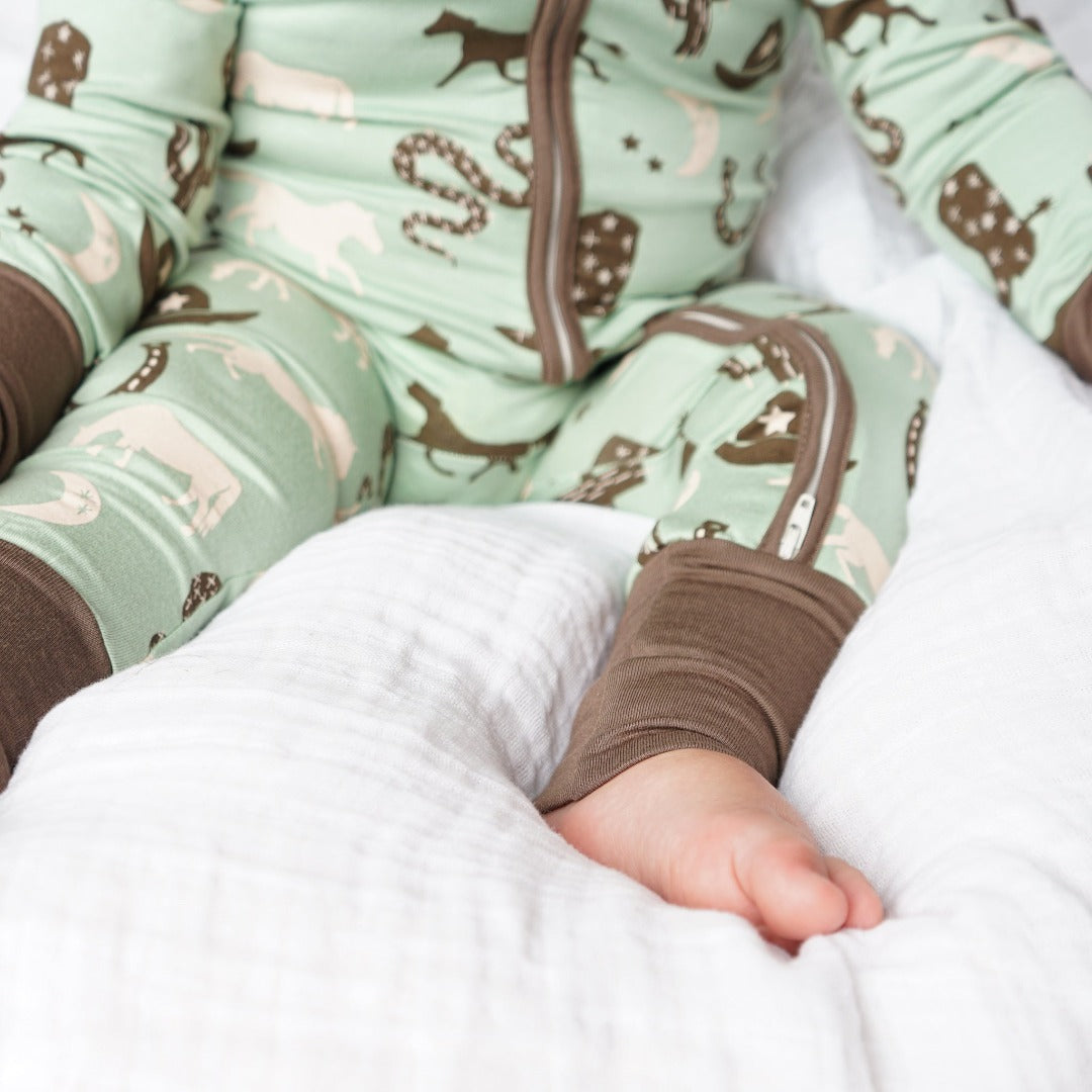 zoomed in photo of a baby's foot. they are wearing the "giddy up" convertible. the "giddy up" print is a western look at horses, cowboy hats, boots, horse rings, cacti, moons and stars. colors on this print include green, brown, and white. 