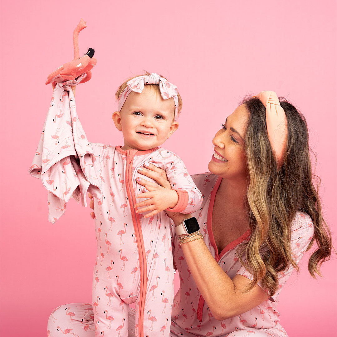 mom and daughter playing with the "fancy flamingo" lovey. the "fancy flamingos" print is a pattern of multiple pink flamingoes scattered around the print. 